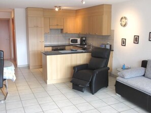 A compact living space with a kitchenette, a black leather chair, a grey sofa, and a small dining table. - Anessa 33 # 4-bed apartment, Bad, WC 4-Bettwohnung, Bad, WC by Interhome (Leukerbad)