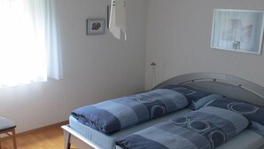 Un dormitorio con cama, una silla y ventana con cortinas.