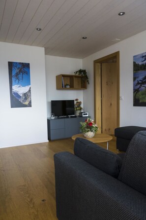 A modern living room with a sofa, a coffee table, and a TV. There is a wooden cabinet with a plant and a painting on the wall. - Albina 40 # 4-bed apartment, Dusche, WC 4-Bettwohnung, Dusche, WC by Interhome (Albinen)