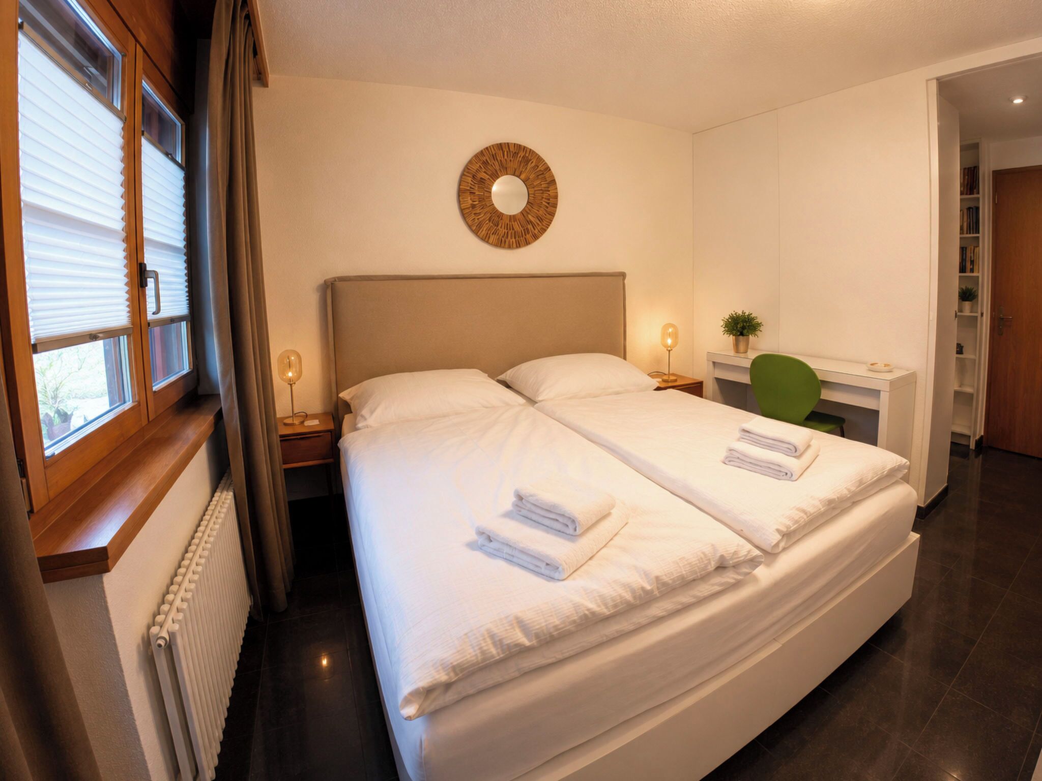 A hotel room with a large bed, a round wall decoration, a desk with a chair, and a radiator.