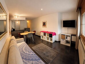 Ein modernes Wohnzimmer mit Sofa, Esstisch, Stühlen, Fernseher und Küchenzeile.