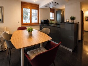 A modern kitchen with a dining table, chairs, and a refrigerator. - Residenz Christina Leukerbad # 5-bed apartment, Dusche, WC by Interhome (Leukerbad)