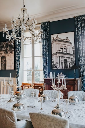 A dining room with a chandelier, a large window, and a framed picture on the wall.