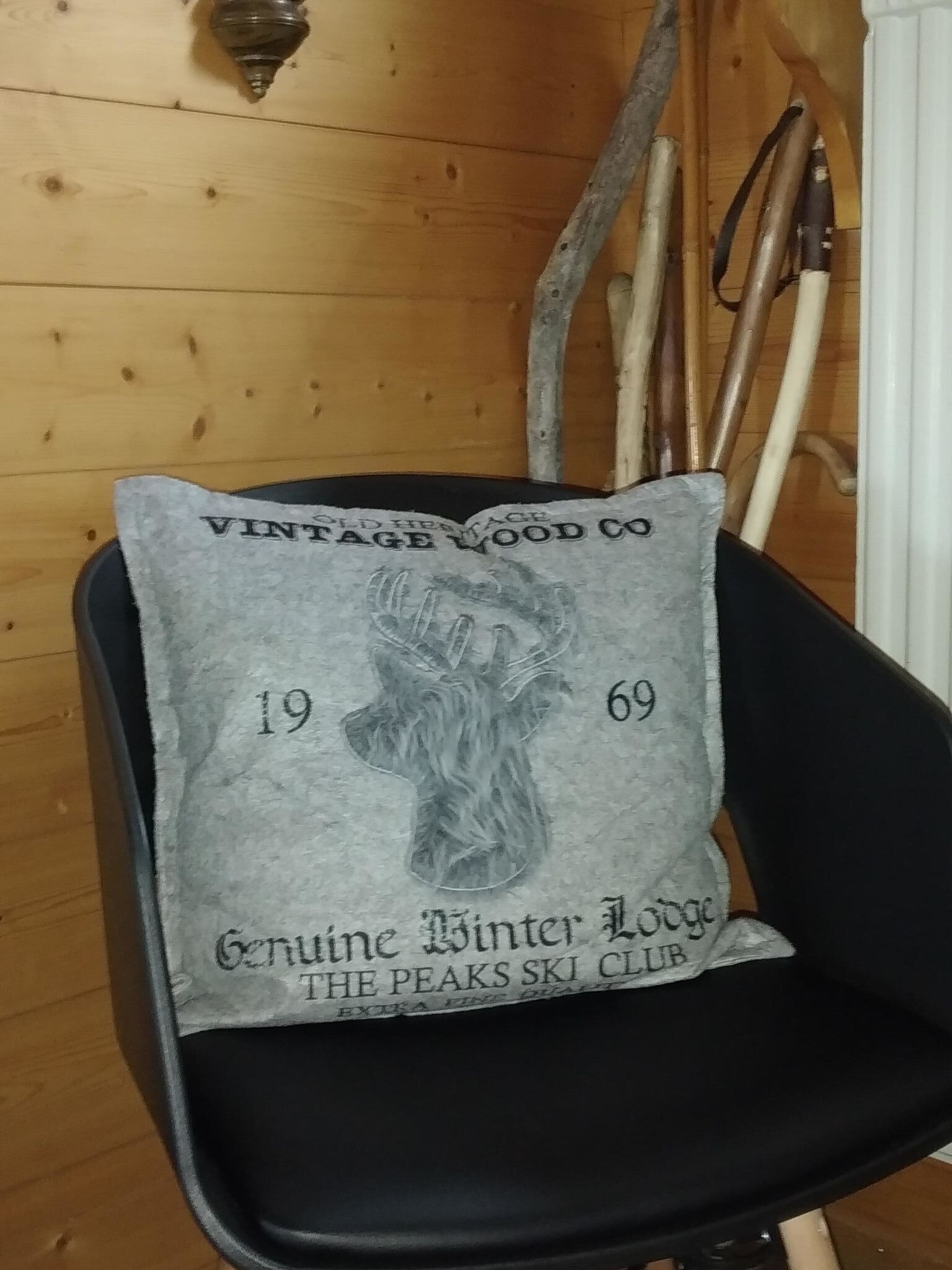 Une chaise noire avec un coussin d’une ancienne entreprise de fabrication de meubles en bois, orné d’un paysage de montagne et du nom d’un club de ski.