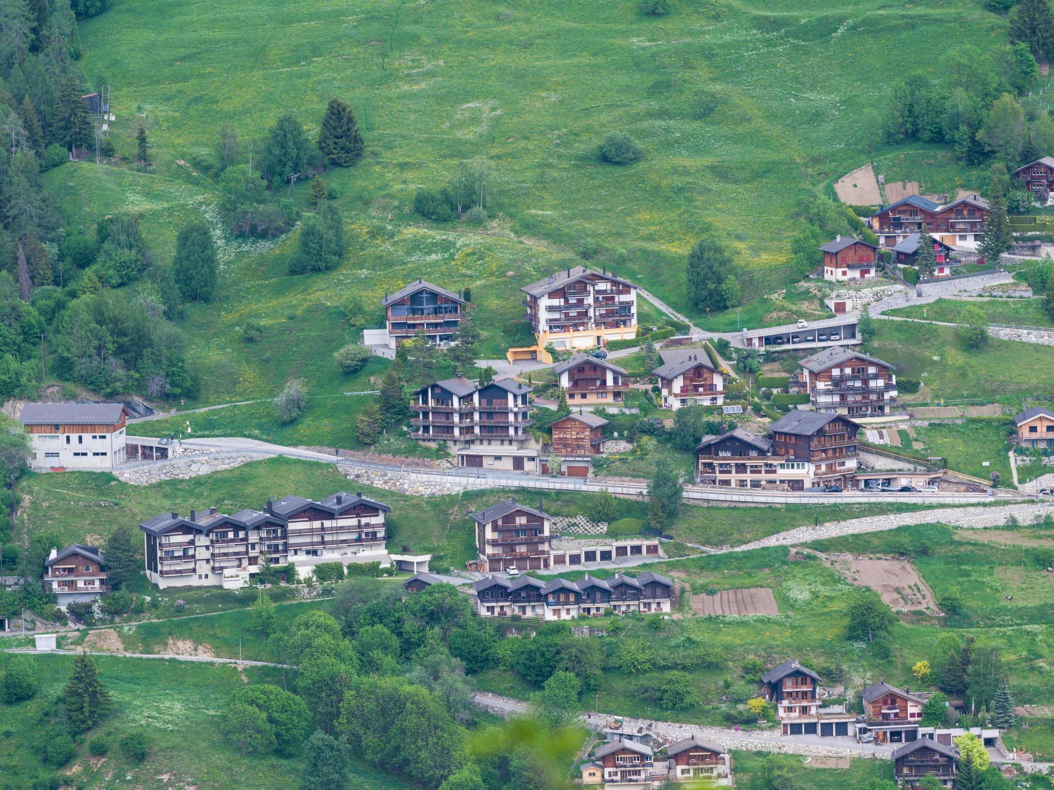 A hillside residential area with multiple multi-story buildings, some with balconies, surrounded by greenery.
