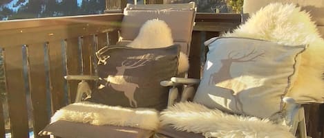 Un balcon avec deux chaises, l’une avec un coussin orné d’un motif de cerf et l’autre avec un coussin représentant la silhouette d’un cerf, ainsi qu’un verre de vin sur une petite table.