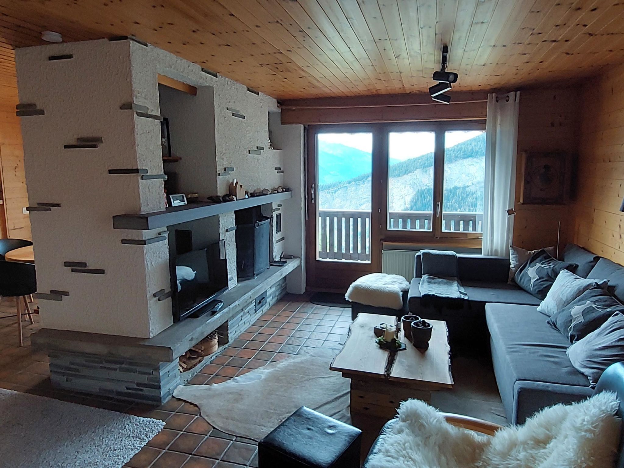 Ein gemütliches Wohnzimmer mit Kamin, einer Couch, einem Couchtisch und Blick auf Berge durch ein großes Fenster.