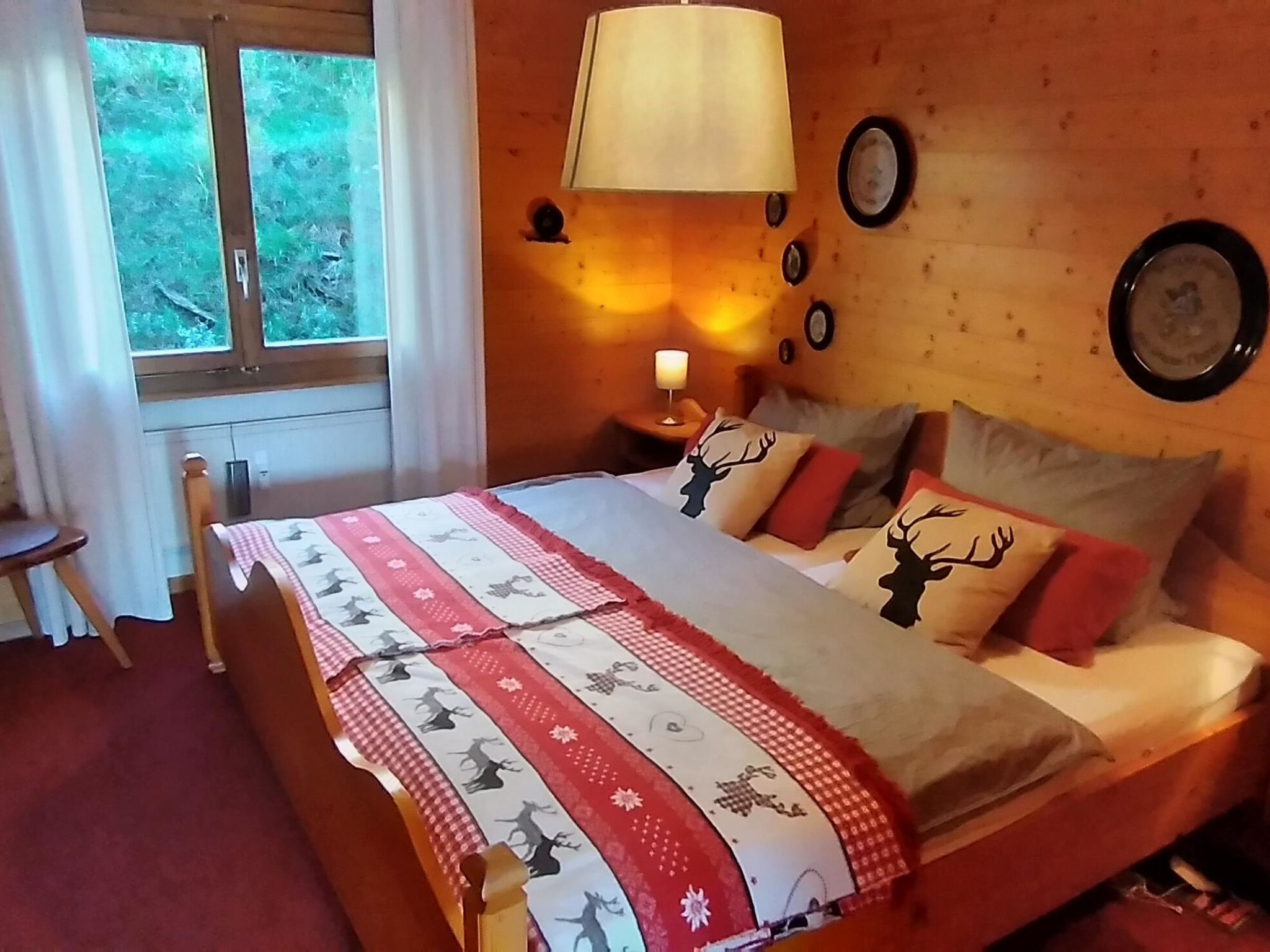 Ein Schlafzimmer mit einem Bett, einem Nachttisch mit Lampe, einem Fenster und einer Wanduhr.