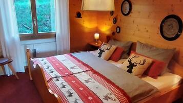 Ein Schlafzimmer mit einem Bett, einem Nachttisch mit Lampe, einem Fenster und einer Wanduhr.
