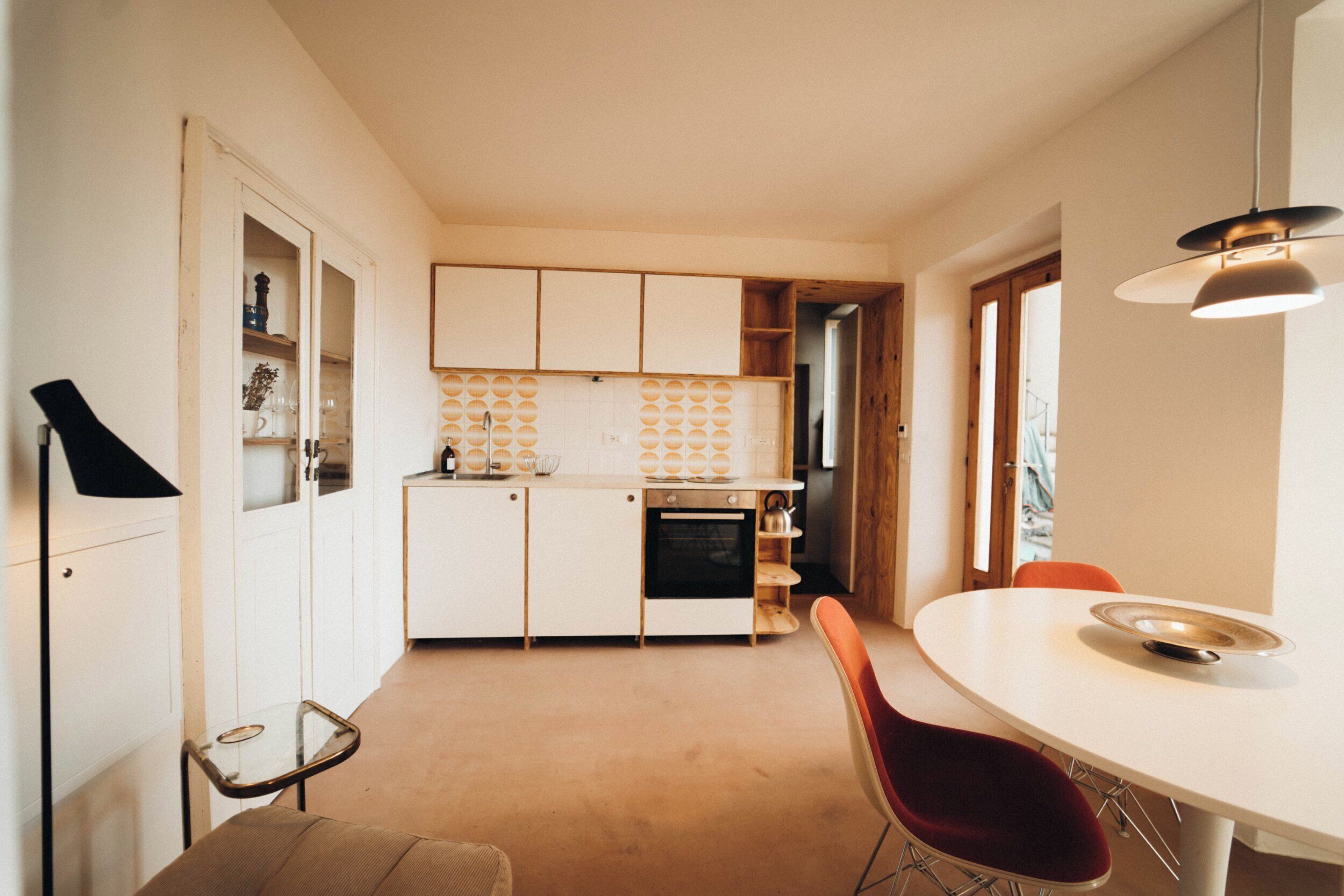 Una cocina compacta con armarios blancos, una mesa de comedor redonda y una silla roja.