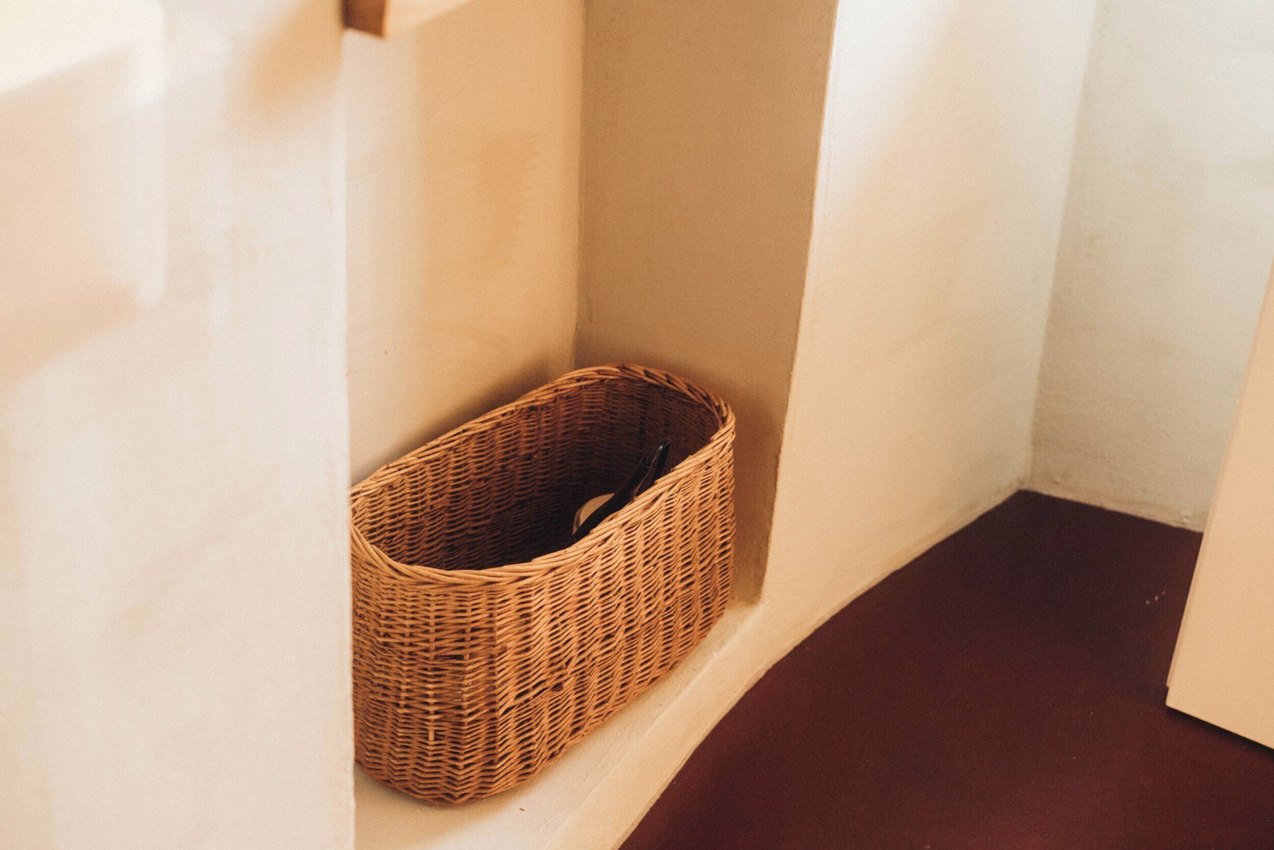 A corner of a room with a wicker basket placed against the wall.