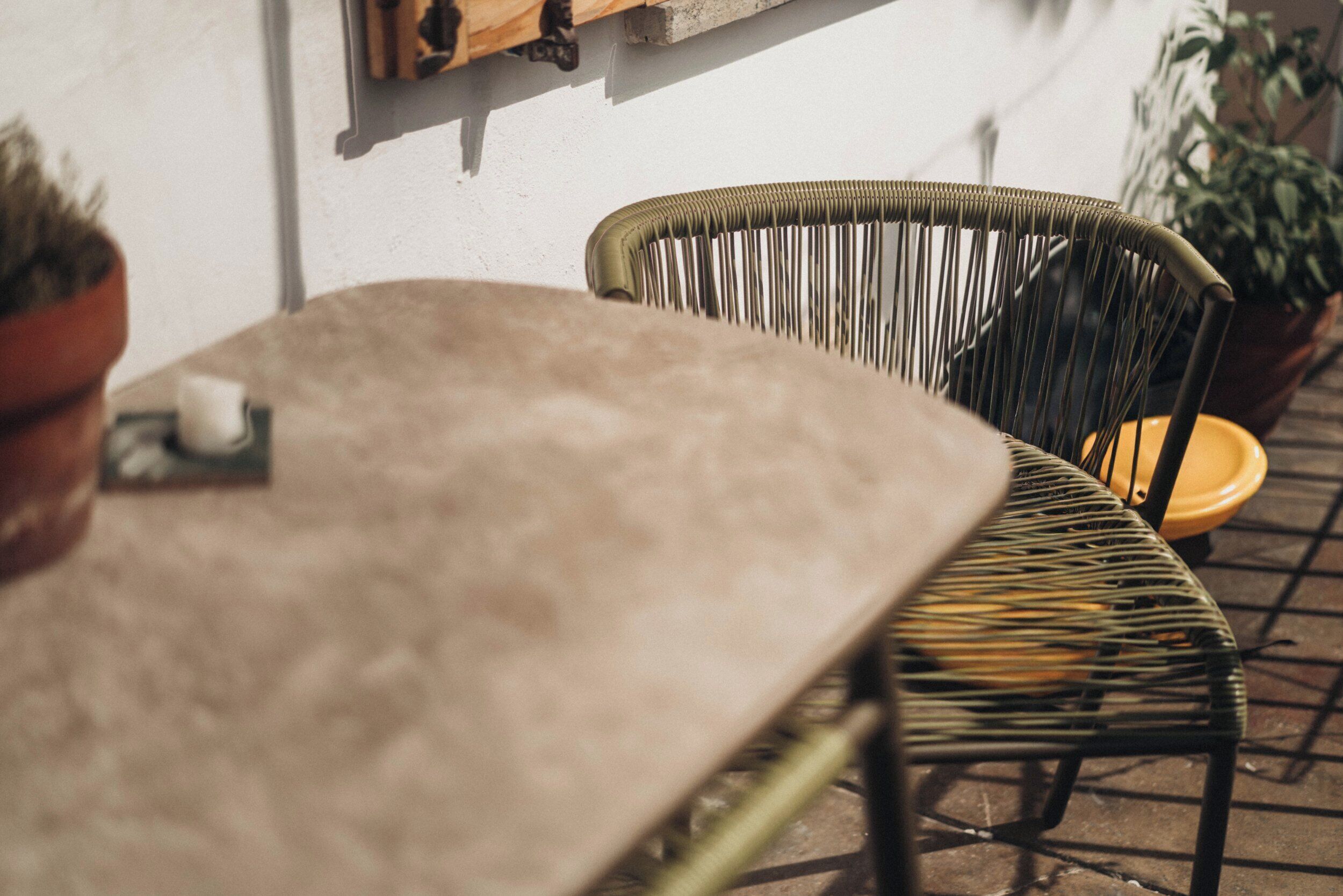 A table with a cushion, a wicker chair, and a potted plant.