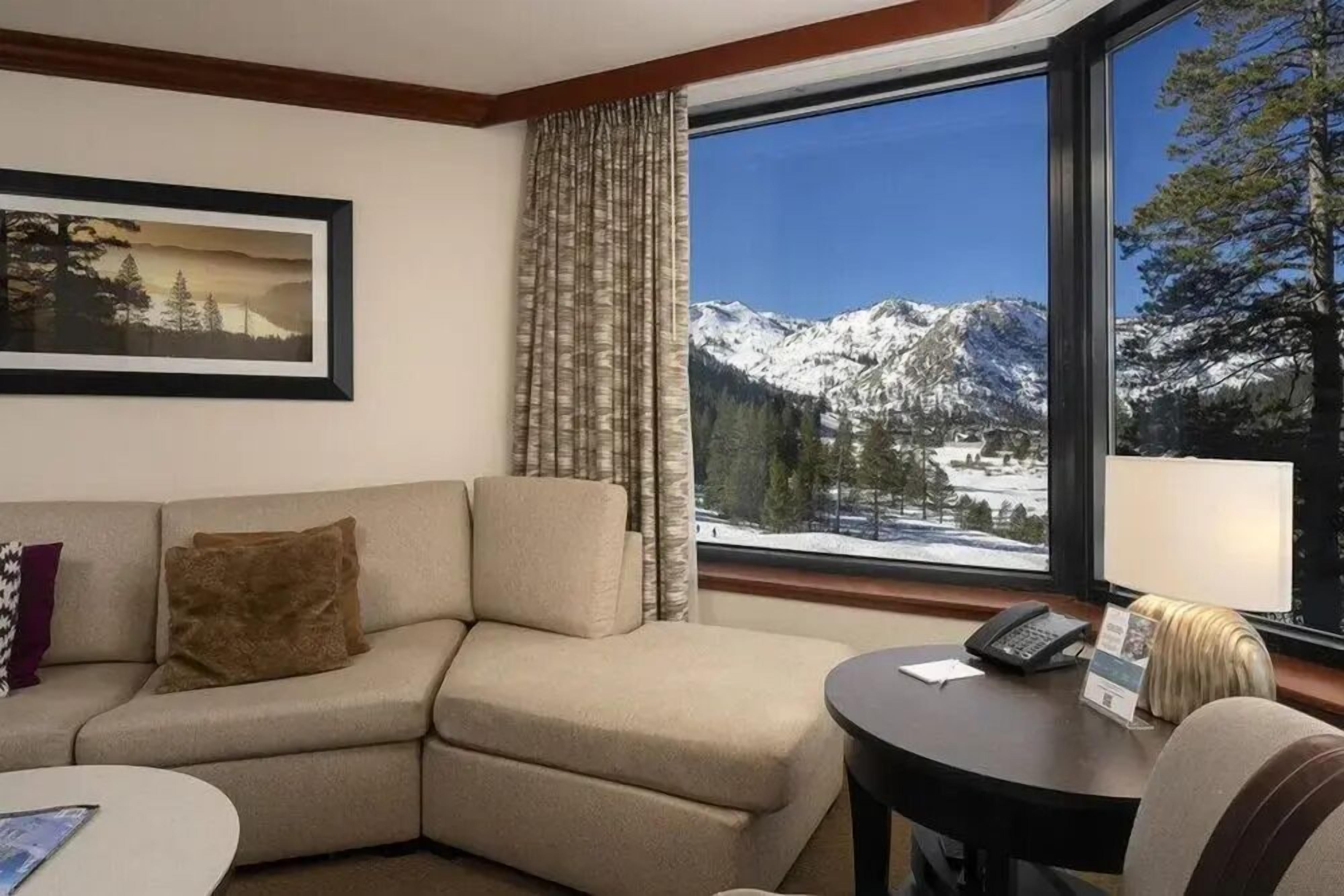A hotel room with a sofa, a small table, a telephone, and a window with a mountain view.