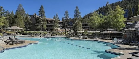 A swimming pool with lounge chairs and umbrellas, surrounded by trees and buildings.