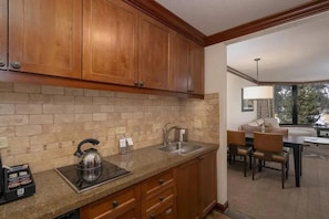 Una cocina con armarios de madera, encimera de granito, tetera y lavabo.