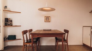 Een eetgedeelte met een houten tafel, vier stoelen, een hangende lamp, een ingelijste foto aan de muur en een kast aan de rechterkant.