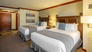 Une chambre d’hôtel avec deux lits, une tête de lit en bois, une table de chevet, une lampe et une porte.