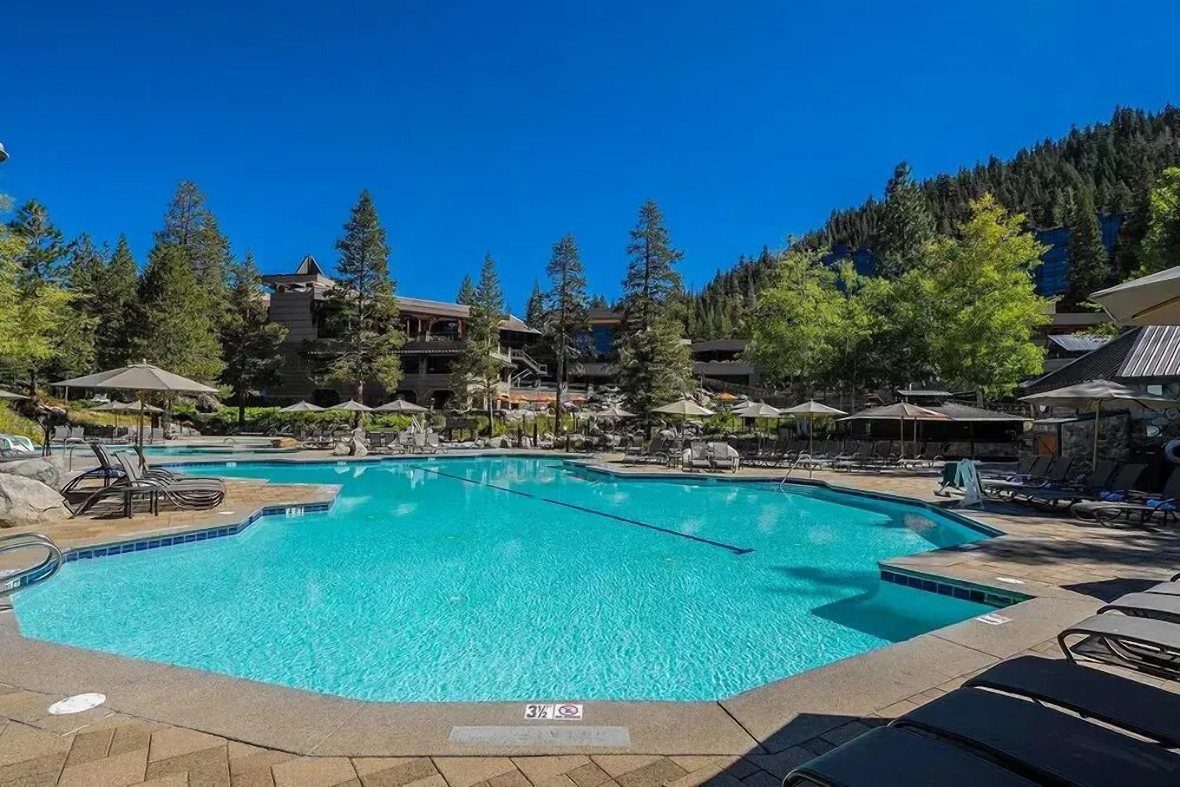 A clear blue pool surrounded by lounge chairs and umbrellas, with a mountainous backdrop.