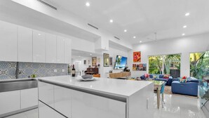 Cozinha moderna com uma ilha grande, sala de jantar com sofá azul e sala de estar com televisão e obras de arte.