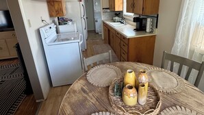 A compact kitchen with wooden cabinets, a white stove, and a dining area with a round table and placemats.