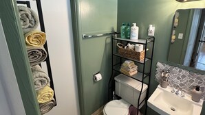 A bathroom with a toilet, sink, towel rack, and shelves with toiletries.