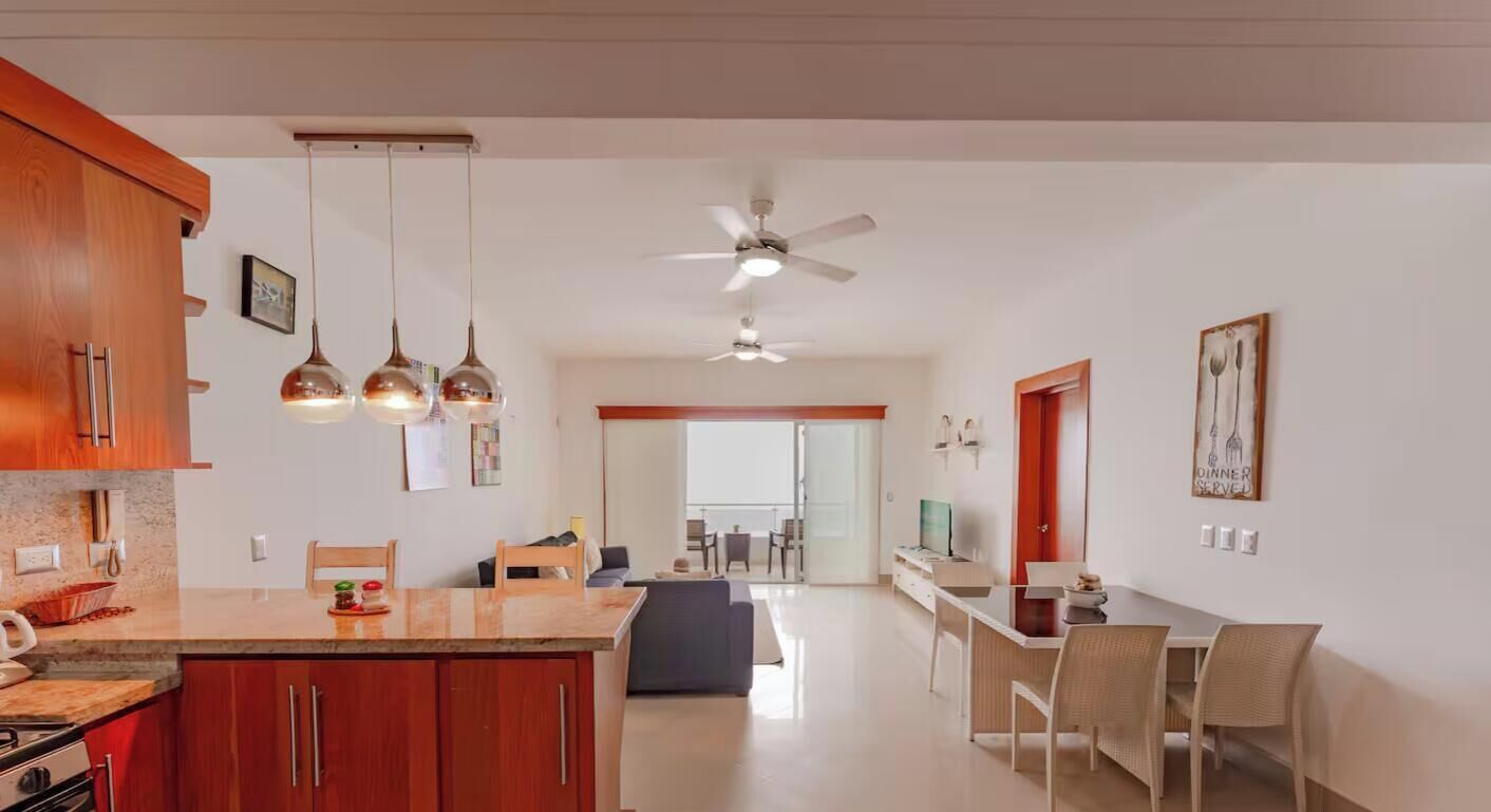 A modern kitchen with a central island, wooden cabinets, pendant lighting, and a ceiling fan.