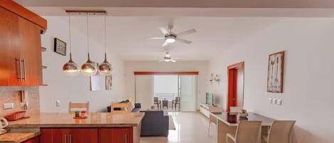 A modern kitchen with a central island, wooden cabinets, pendant lighting, and a ceiling fan.