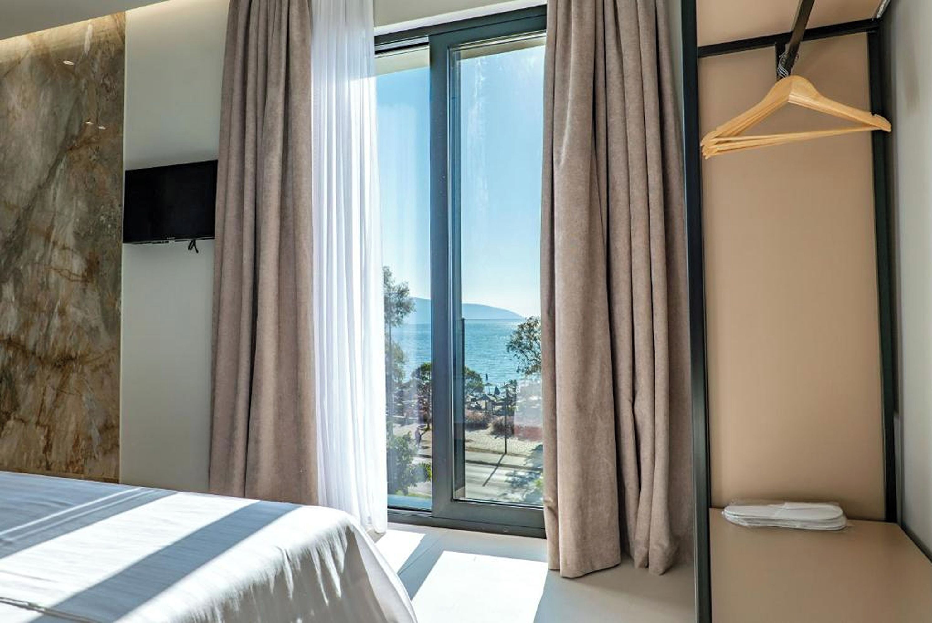Un dormitorio con cama, televisor, ventana con cortinas y vista al mar.