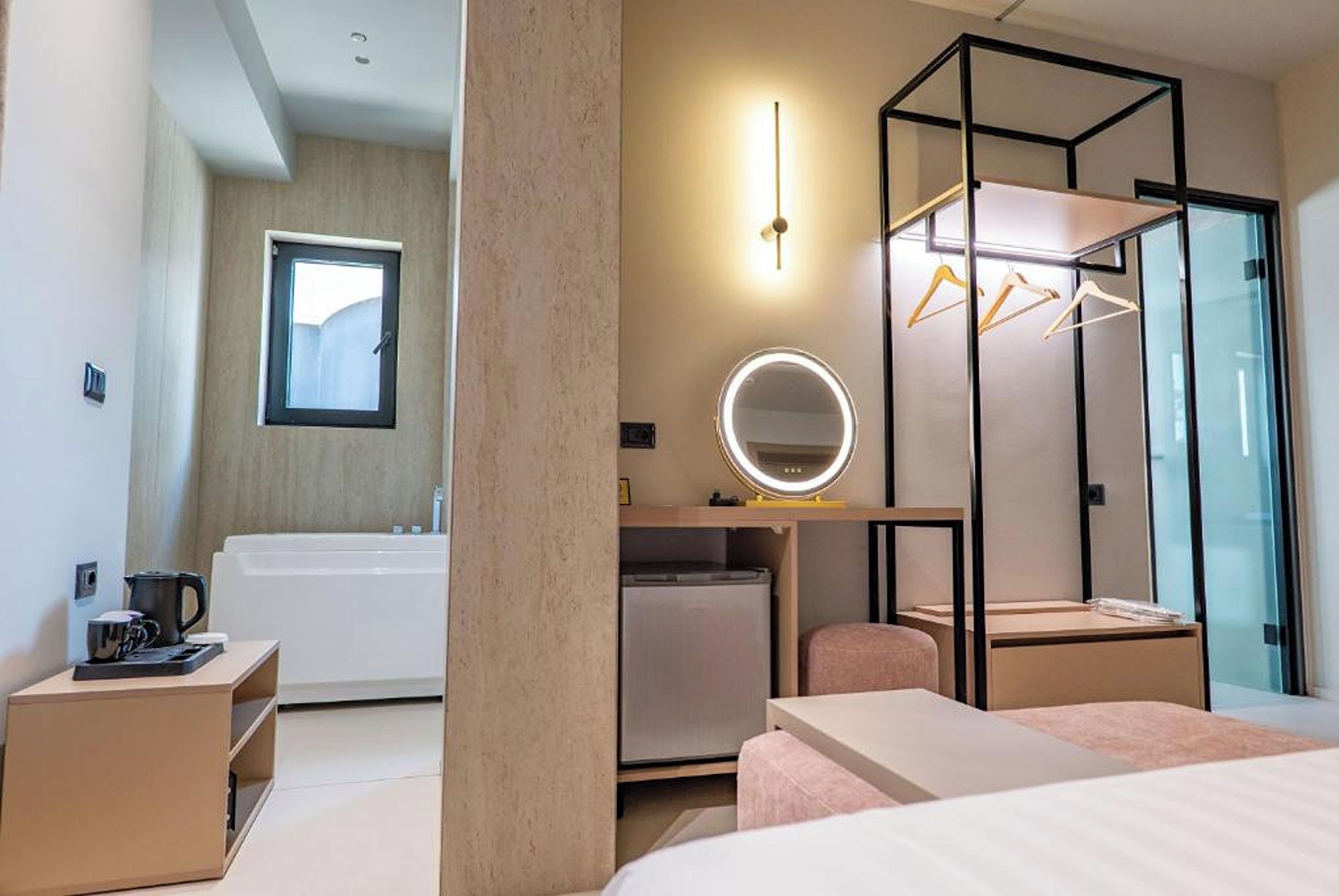 Habitación de hotel moderna con cama, escritorio, espejo, perchero y vista al baño.