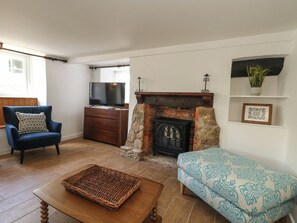 A living room with a blue armchair, a wooden coffee table, a fireplace, a television, and a framed picture on the wall. - Greenwich Cottage (Bridport)