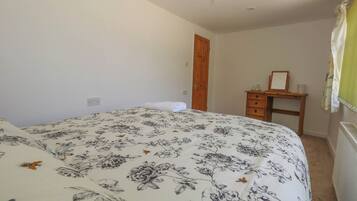 A bedroom with a floral bedspread, a wooden dresser, a mirror, and a radiator.