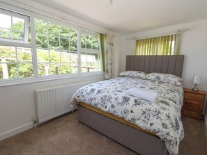 A bedroom with a bed, a window, a radiator, and a nightstand with a lamp. - Greenwich Cottage (Bridport)