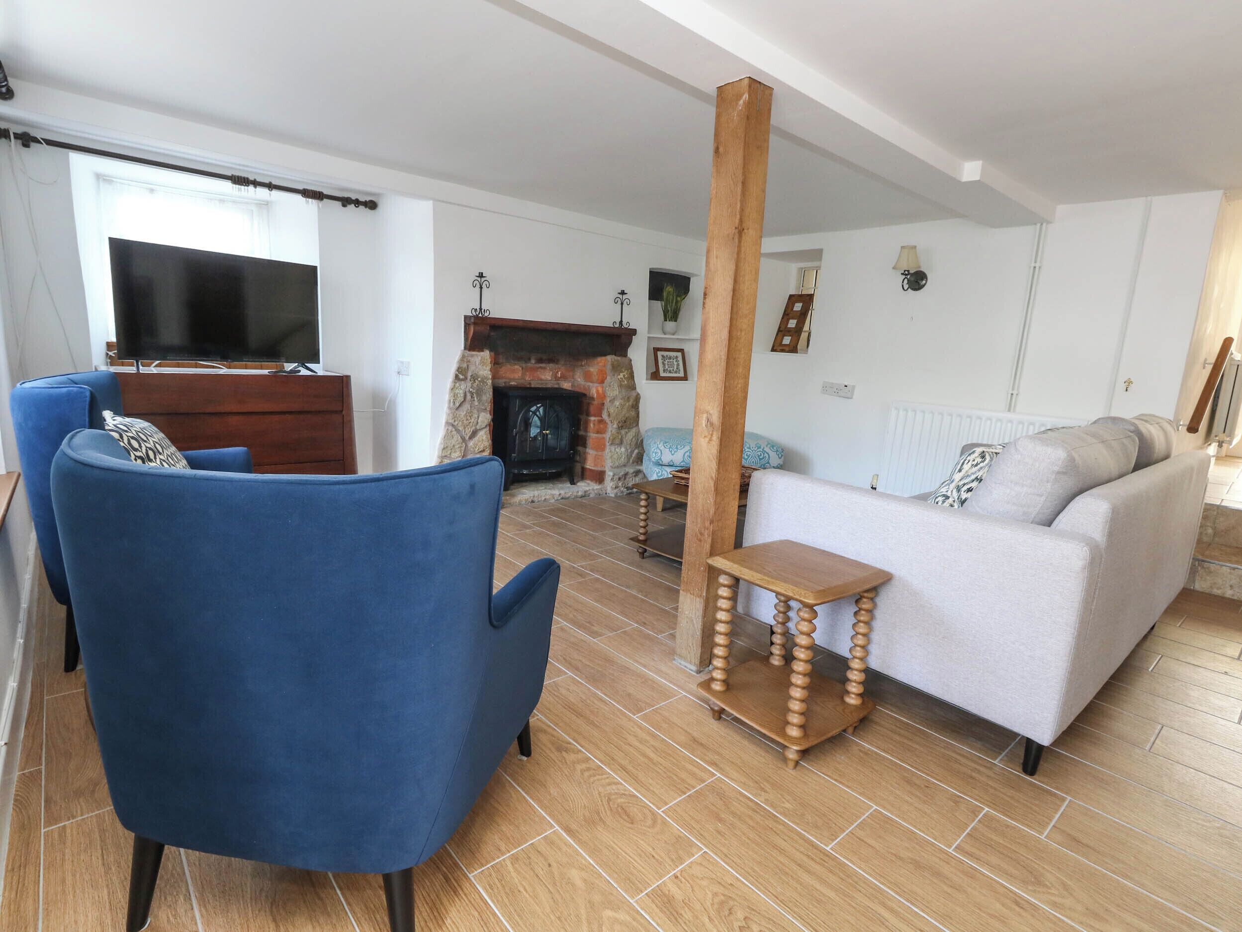 A living room with a blue armchair, a grey sofa, a wooden coffee table, a fireplace, and a television.