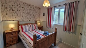 A bedroom with a wooden bed, striped bedding, two bedside tables with lamps, a patterned wallpaper, and a window with curtains.