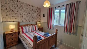 Une chambre à coucher avec un lit en bois, une literie à rayures, deux tables de chevet avec des lampes, un papier peint à motifs et une fenêtre avec des rideaux.