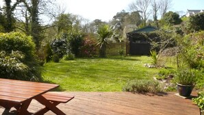 Una terrassa de fusta amb taula de picnic, gespa ben cuidada i zona de jardí tancada.
