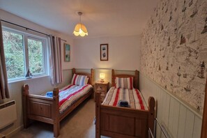 Ein Schlafzimmer mit zwei Holzbetten, einem fenster mit Vorhängen, einer Wand mit Segelmotivem und einer hängenden Leuchte.