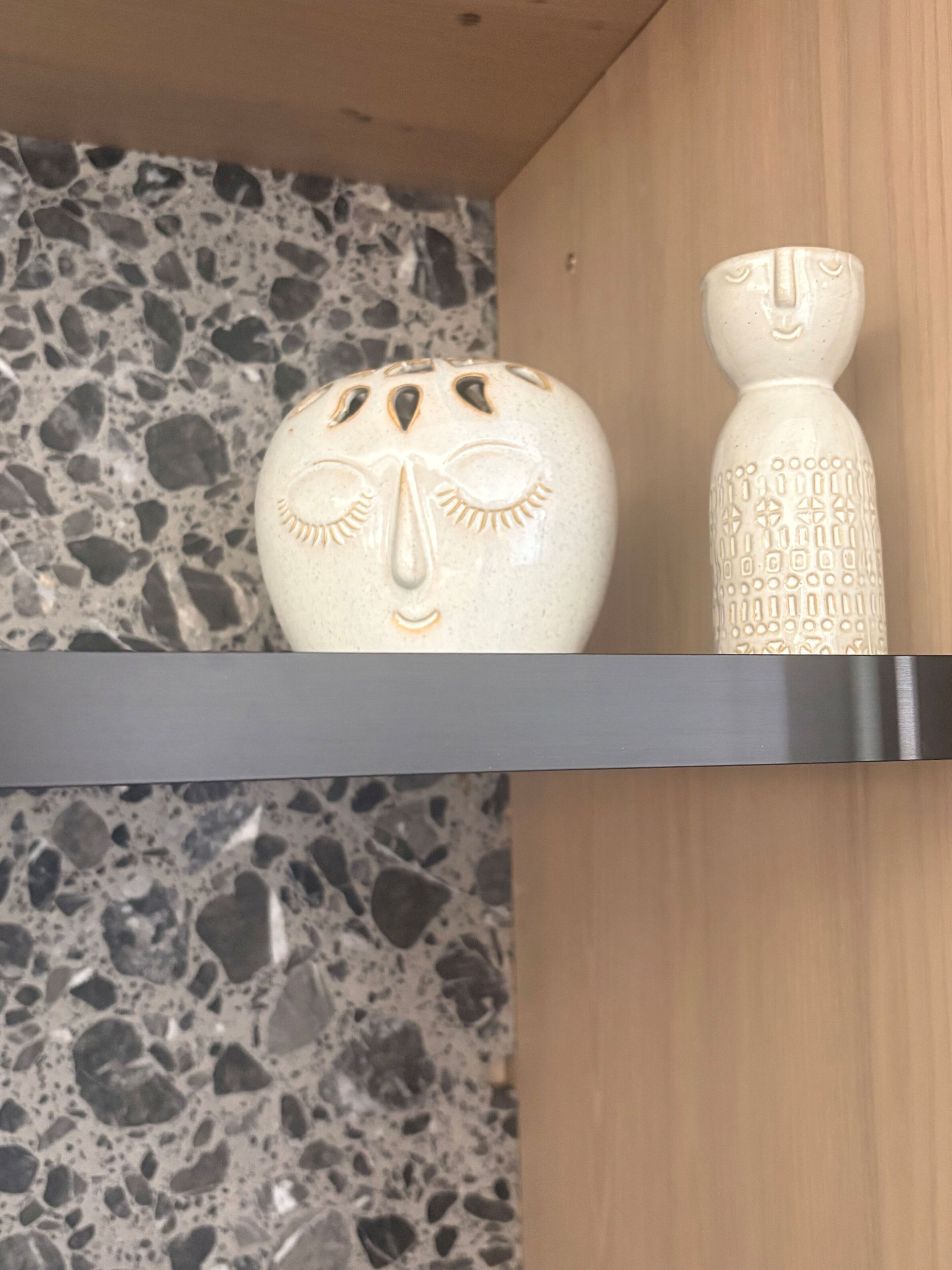 A shelf with two ceramic vases against a terrazzo floor and wooden panel backdrop.