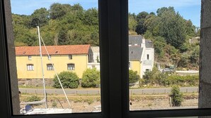 Blick durch ein Fenster auf ein Gebäude, ein Segelboot und eine Anlegestelle mit Booten.