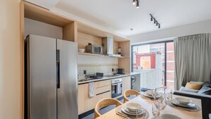 A compact kitchen with a refrigerator, microwave, and stove, a dining table set with plates and glasses, and a window with a view of a building. - Myla - Loft in Condesa (Mexico City)