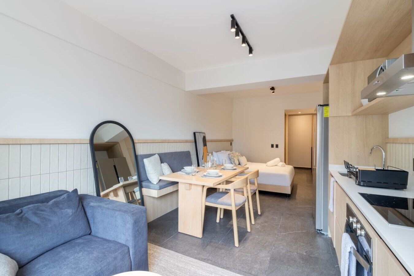 A modern hotel room with a dining area, kitchenette, and a large mirror.