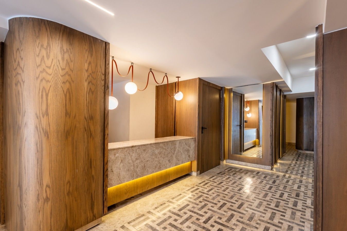 En moderne hotellobby med receptionsdisk, træpaneler og mønstret gulv.