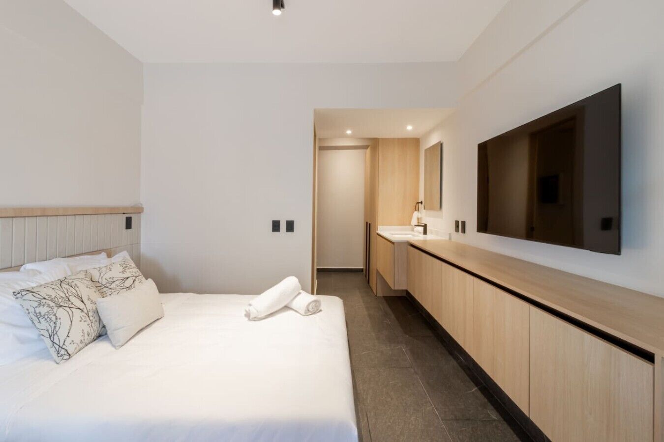 A modern hotel room with a large bed, a bathroom with a mirror, and a flat-screen TV.