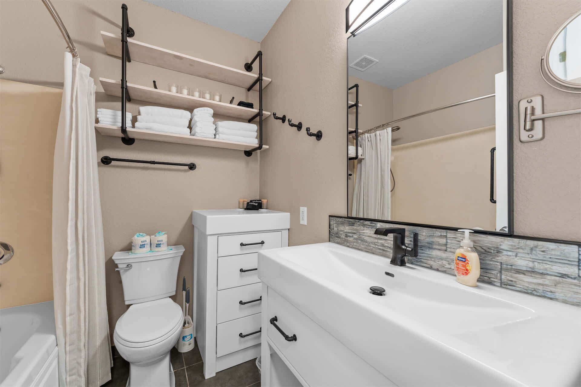 A bathroom with a toilet, a sink with a mirror, and shelves with towels.