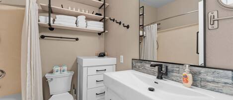 A bathroom with a toilet, a sink with a mirror, and shelves with towels.