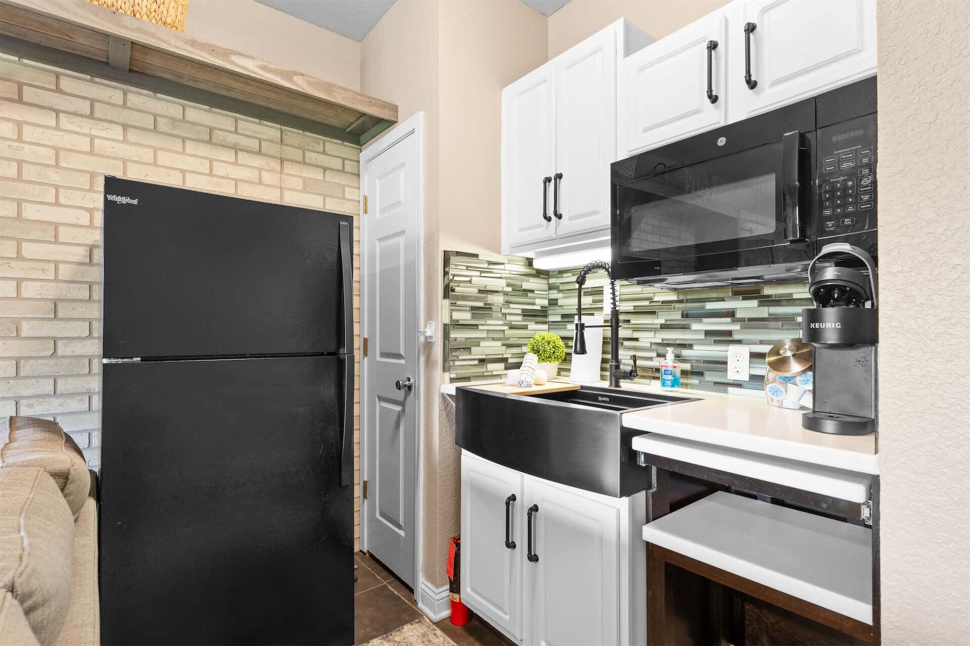A compact kitchen with a black refrigerator, white cabinets, a black microwave, and a coffee maker.