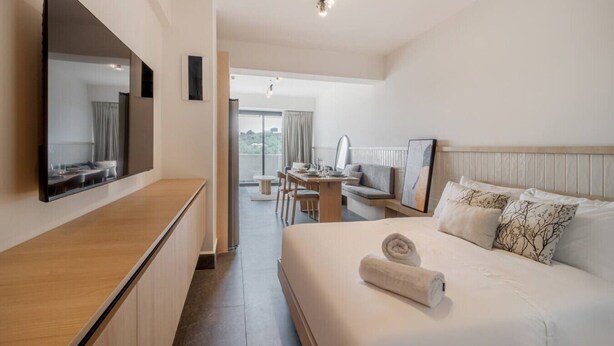 Ett hotellrum med en säng, ett skrivbord, en stol, en stor spegel och utsikt över omgivningarna.