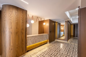 Un hall d’hôtel moderne avec un comptoir d’accueil, des panneaux de bois et un revêtement de sol à motifs.