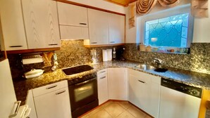 Eine Küche mit weißen Schränken, einer Arbeitsplatte aus Granit, einem eingebauten Backofen und einem Fenster mit dekorativem Gittermuster.