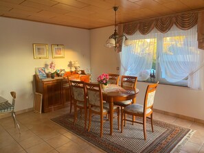 A dining area with a wooden table and chairs, a chandelier, and a window with sheer curtains. - Chalet Kristall # 6-bed apartment, Dusche, WC 6-bed apartment, Dusche, WC by Interhome (Albinen)